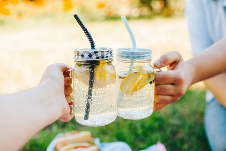 人们在一个质朴的木质背景下, 用两瓶自制柠檬汁的梅森玻璃瓶举杯祝酒。
