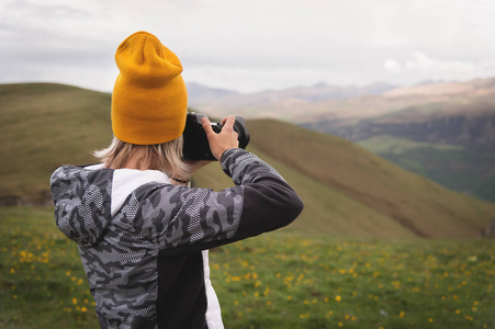 一个年轻的女孩在一个多云的日子里在高山上拍摄高原的照片。在后面的女孩的看法