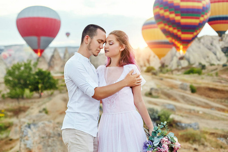 情侣在爱站立在气球的背景在里。山上的男人和女人看着许多飞行气球。土耳其的童话风光的山脉。自然婚礼
