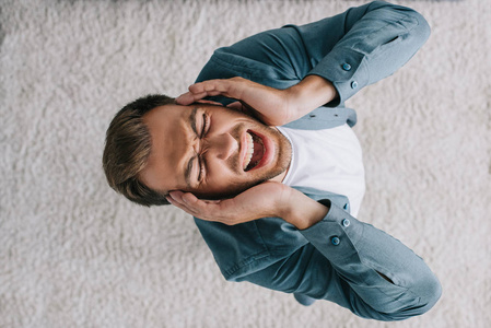 年轻男子尖叫和头痛在家中的头顶观照片