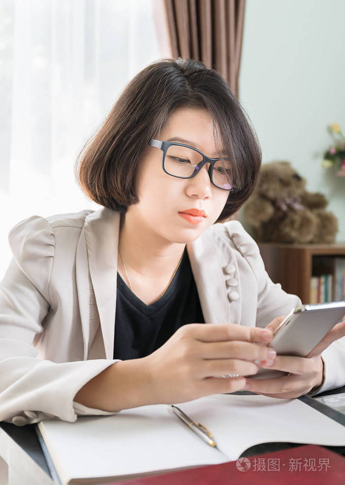 年轻女孩的短发在智能休闲穿着笔记本电脑, 而坐在窗口附近的家庭办公