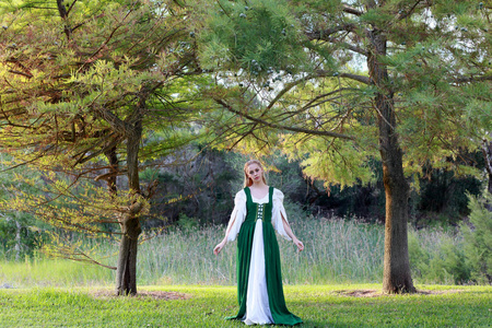 身穿绿色中世纪长袍的金发女郎全长画像, 在森林中游荡