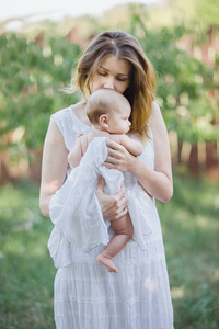 一个美丽的年轻母亲抱着一个婴儿在她的怀里站在花园里