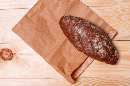 美味的黑色面包和纸袋在木质背景。从上面查看。文本空间