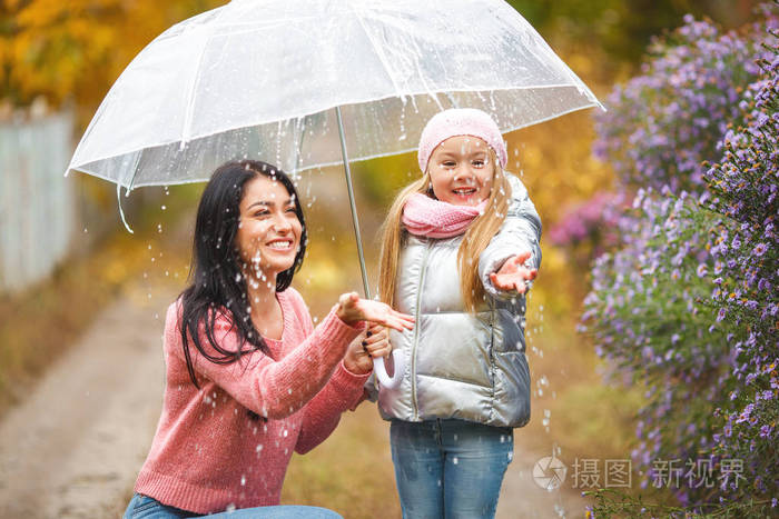 可爱的孩子与她的年轻母亲在秋季背景下的雨伞乐趣愉快的家庭在秋天