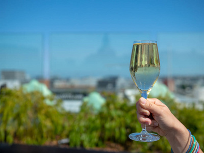 女人手捧着一杯白葡萄酒在阳光明媚的日子里, 背景是城市天际线照片