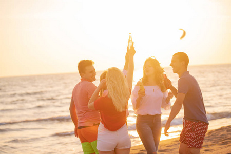 一群快乐的年轻人在海滩上喝着美丽的夏日日落