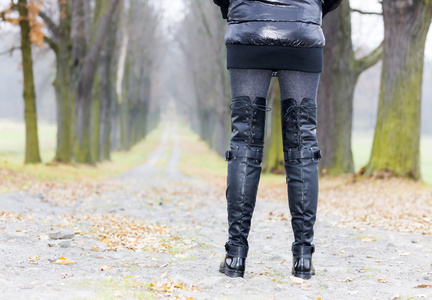 在秋季巷子里穿黑色的衣服和靴子的女人的细节