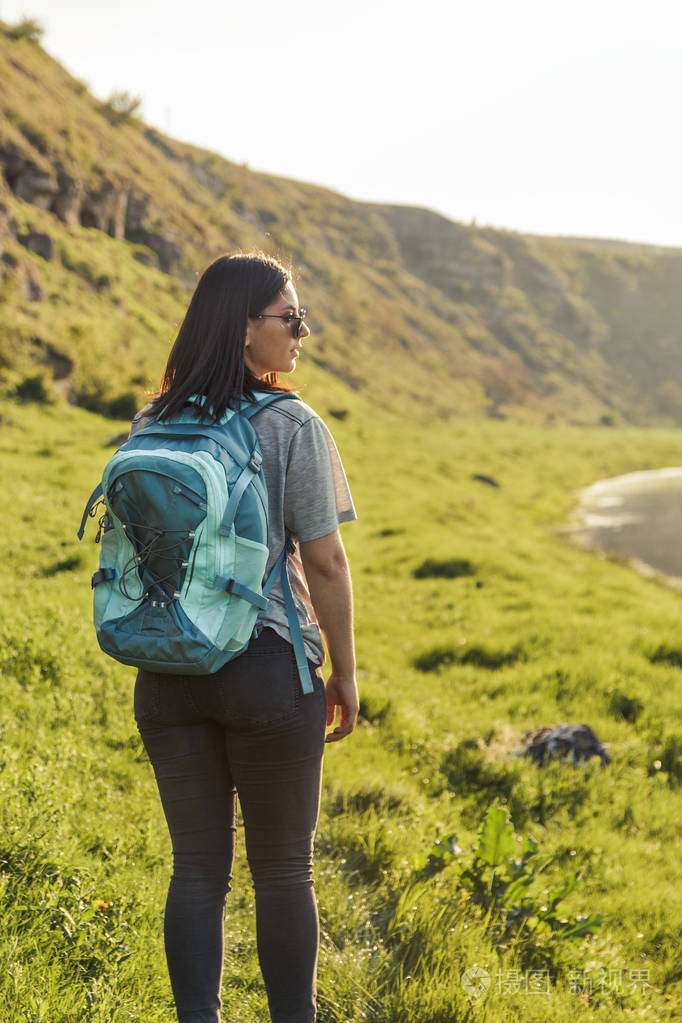 旅行妇女与背包看风景在自然绿色领域在日落旅游业概念