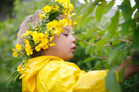一个穿着黄色雨衣的小孩子和一个毛茛的花圈从灌木丛中吃浆果。
