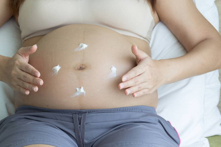 孕妇洗手液帮助皮肤腹部在卧室的背景, 健康的概念