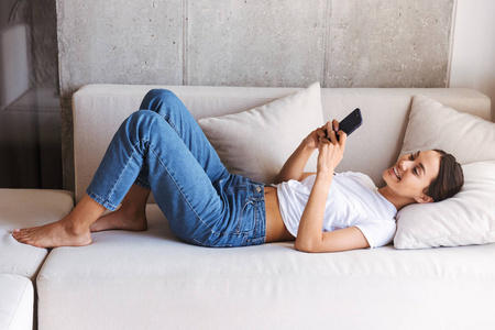 在家里躺在沙发上的快乐年轻的亚洲妇女使用手机照片