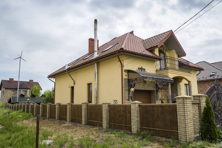 新的黄色两层住宅小屋, 有瓦顶,前廊,塑料窗,高烟囱,蓝天背景阳台.