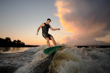 黄昏时分, 年轻的男子 wakesurfing, 在美丽的阴天的背景下波浪。