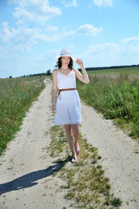 穿着白色连衣裙和白色帽子的女孩, 在波兰举行户外摄影会。年轻女性走在土路
