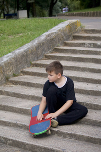 一个有滑板的少年。坐在一个滑板的背景下的石头楼梯