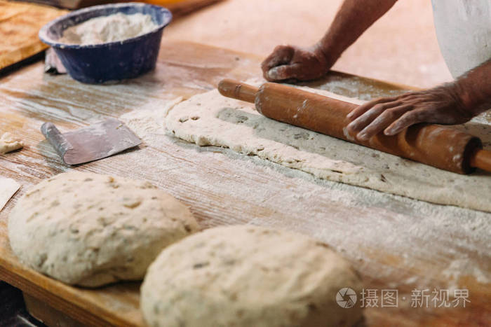 男面包师准备面包。贝克用面粉揉面团。做面包。乡村传统风格的面包店