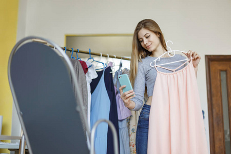 美丽微笑女孩手拿着新衣服在现代缝纫车间用手机拍照照片