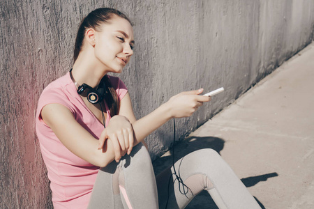 运动的年轻女孩在粉红色的 t恤上休息后, 在阳光下运行, 手持手机在她的手
