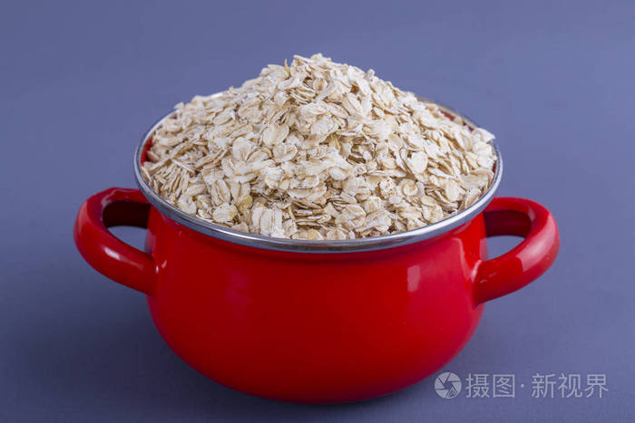 红色平底锅与干燥燕麦片在灰色背景。关门了概念健康饮食