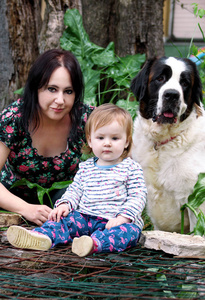家庭和爱宠物概念肖像与母亲和女婴是坐和玩狗在花园户外。儿童和母亲与 st. 伯纳德狗摆姿势, 四周绿树和灌木