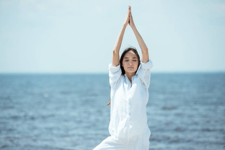 亚洲妇女闭上眼睛站在体式 vrikshasana 树形姿势 在海滩上的海上