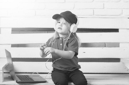孩子听音频。在白色背景下的笔记本电脑旁边戴着耳机的小孩