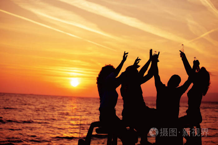 日落时海滩派对上年轻人的剪影