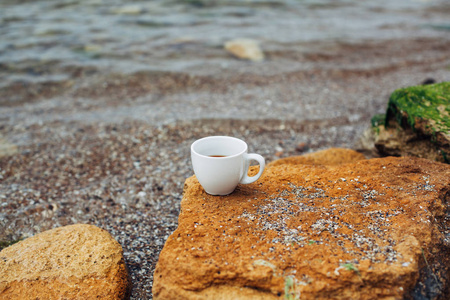 杯咖啡在海水和石头的背景。海新鲜早晨概念