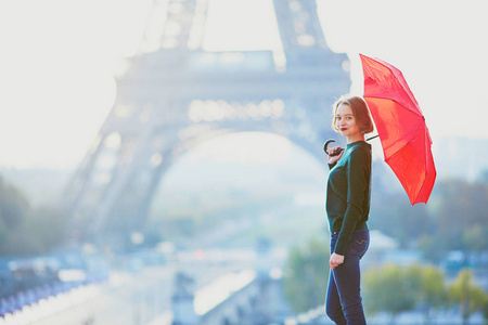 美丽的年轻女孩与红色雨伞在巴黎埃菲尔铁塔附近的早晨