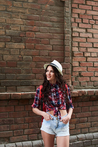 女子游客手持口袋短裤, 而站在街上的红砖墙上