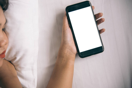 亚洲妇女手用智能手机在卧室里的空白屏幕在早晨