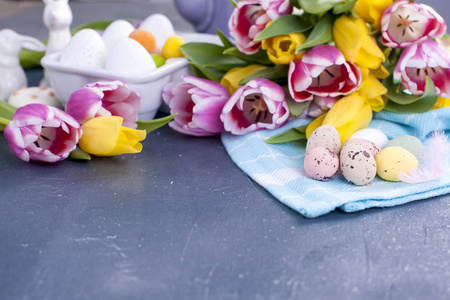 复活节贺卡与彩色鹌鹑鸡蛋糖果蓝色针织餐巾和郁金香花。具有复制空间的春季假日概念