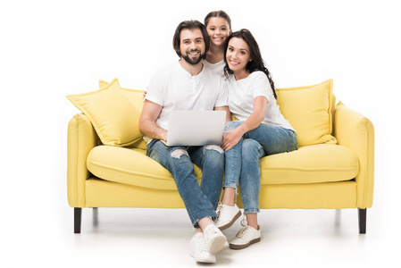 微笑的家庭与笔记本电脑坐在黄色的沙发上孤立的白色