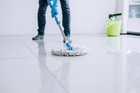 丈夫的家务和清洁的概念, 快乐的年轻人在蓝色橡胶手套擦拭灰尘使用拖把, 而在家清洁地板上