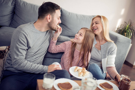 幸福的年轻家庭的肖像在家里一起吃早饭。家庭, 食品, 饮料和人的概念