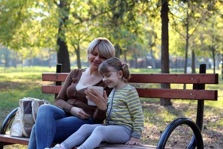 母亲和女儿坐在公园和戏剧与平板电脑