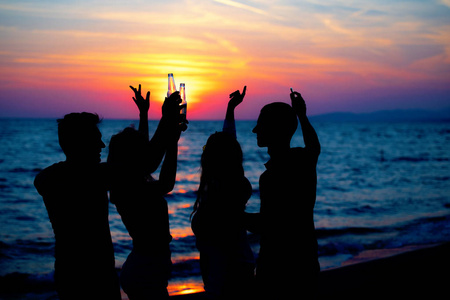 日落时海滩派对上年轻人的剪影