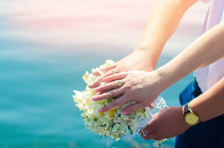 特写新娘和新郎的手与结婚戒指和花束。爱情和婚姻。在河的背景婚礼配件和装饰