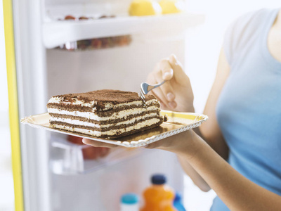 从冰箱中摄取美味的高卡路里甜点的女人, 节食失败和不健康的食物概念