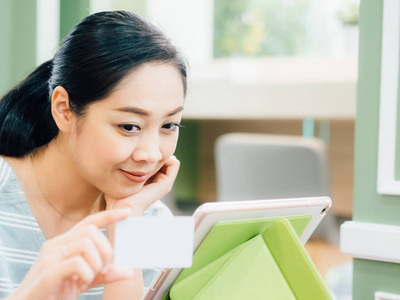 快乐亚洲妇女使用白色样机信用卡在线购物平板电脑