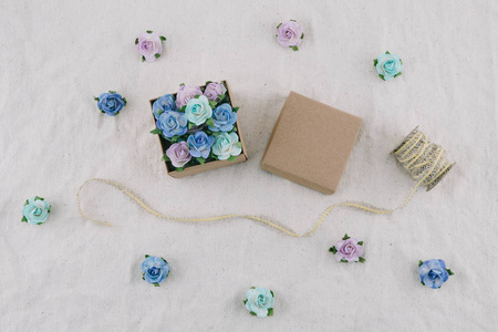 棕色礼品盒和绳子装饰用蓝色色调纸花在薄纱织物上, 选择性地聚焦在盒子里的花上