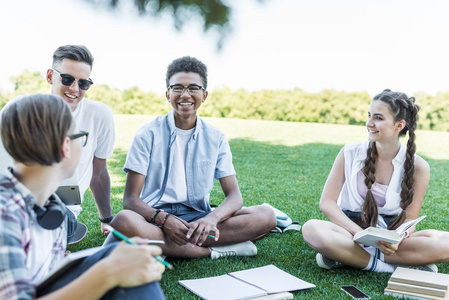 快乐的多民族青少年学生坐在草地上一起学习在公园里