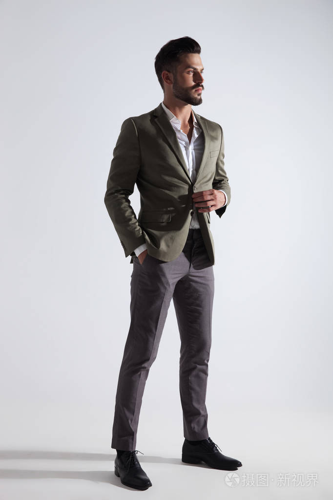 穿着灰色西装的优雅男子站在浅灰色的背景上, 看着侧面, 全长图片