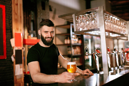 工艺啤酒。酒吧柜台的酒保在酒吧里拿着啤酒喝着玻璃高分辨率