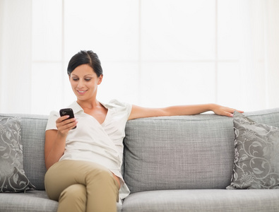 快乐的年轻女子坐在沙发上和读短信的手机皮套