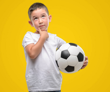 黑头发的小孩玩足球严肃的脸思考问题, 非常困惑的想法