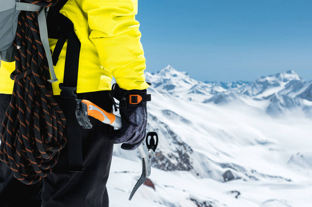一个登山运动员在积雪覆盖的群山中手持一把冰斧。从后面特写。利用登山设备进行户外极限户外攀岩运动