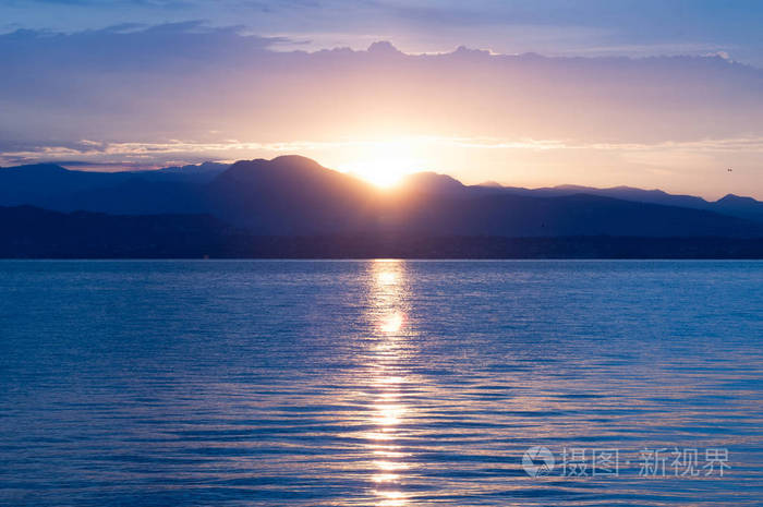湖上日出清晨的全景山在剪影和上升的耀眼的太阳的光芒在意大利的