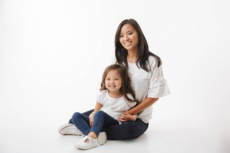 可爱的年轻的亚洲妇女母亲的形象与她的小女孩的女儿坐在白色的墙壁背景隔离